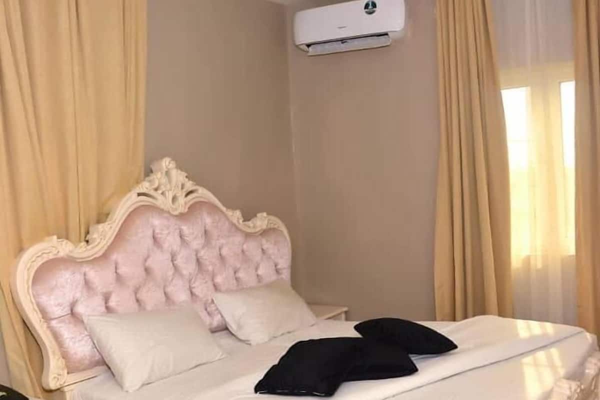 Una cama con cabecera capitonada, dos almohadas y una mesita de noche con una lámpara.