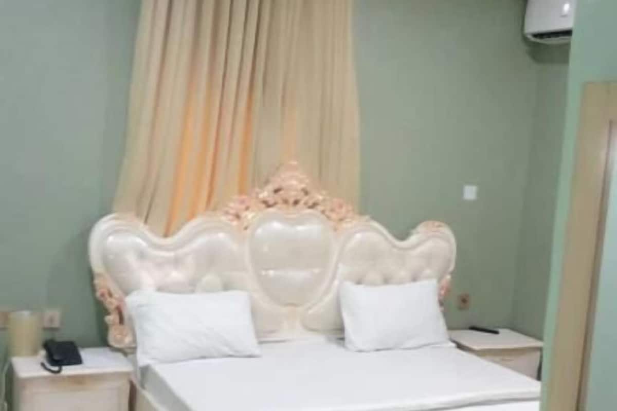 Un dormitorio con una cama grande, una mesita de noche, aire acondicionado en la pared y una cortina.
