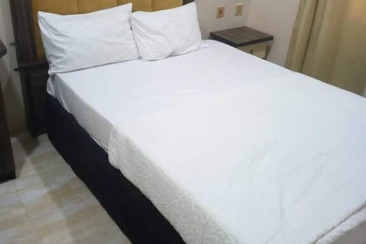 Una cama bien hecha con ropa blanca, cabecera de madera y una mesita de noche.