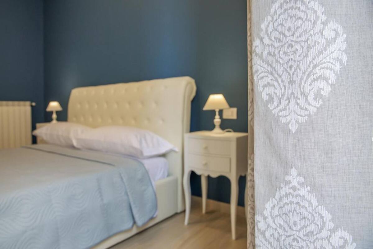 Quarto com cama, duas mesas de cabeceira com abajures e uma parede azul.