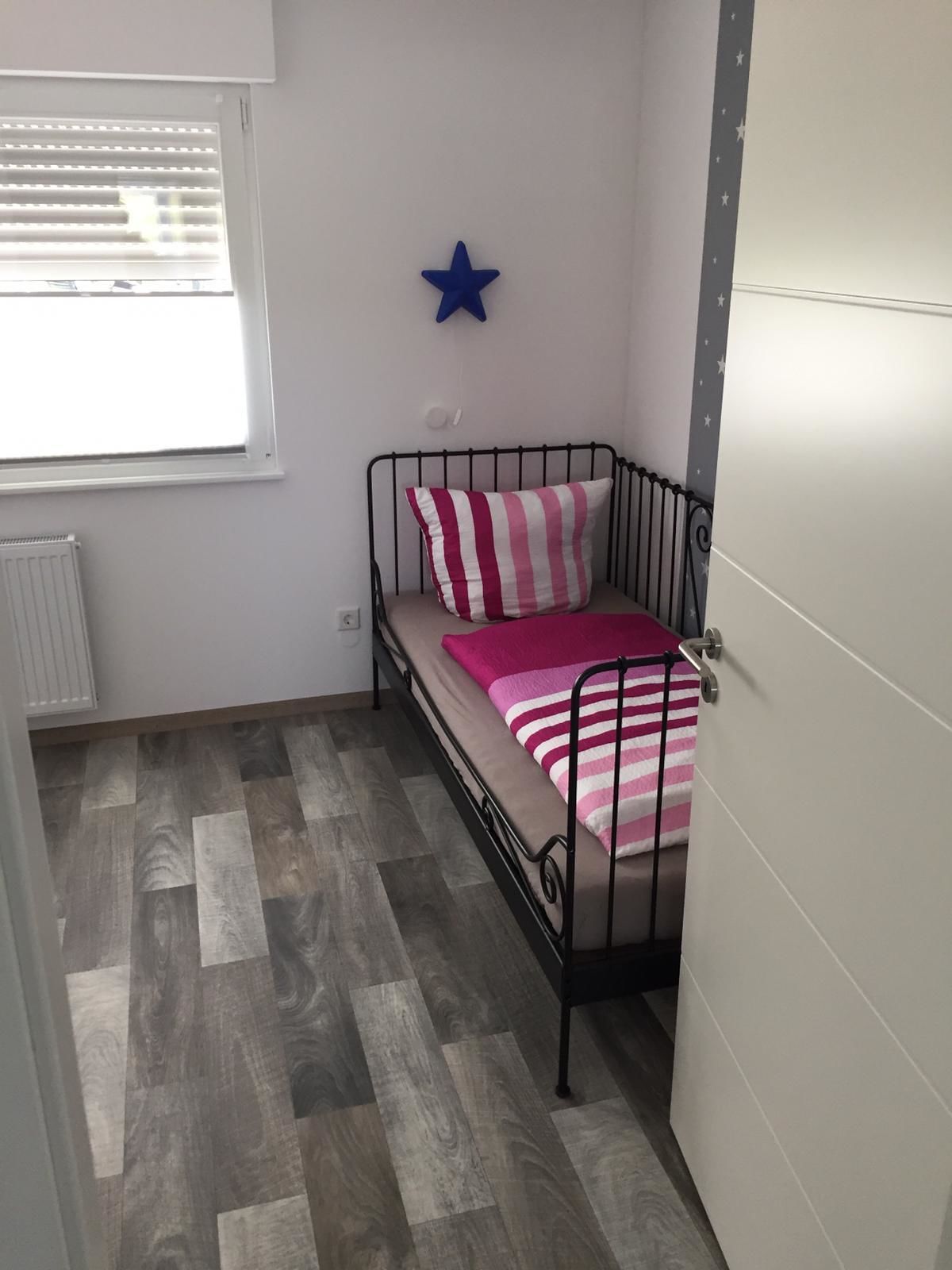 A small, single-bed room with a metal frame, a striped pillow, and a star decoration on the wall.