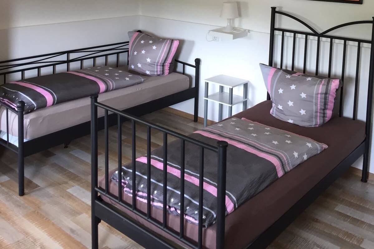 Une chambre avec deux lits simples, un luminaire suspendu blanc, une petite table ronde et deux tableaux accrochés aux murs.