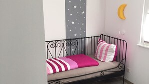 Une petite pièce chaleureuse, avec un lit simple, un mur décoré de motifs d’étoiles, un ornement en forme de croissant de lune et une fenêtre.