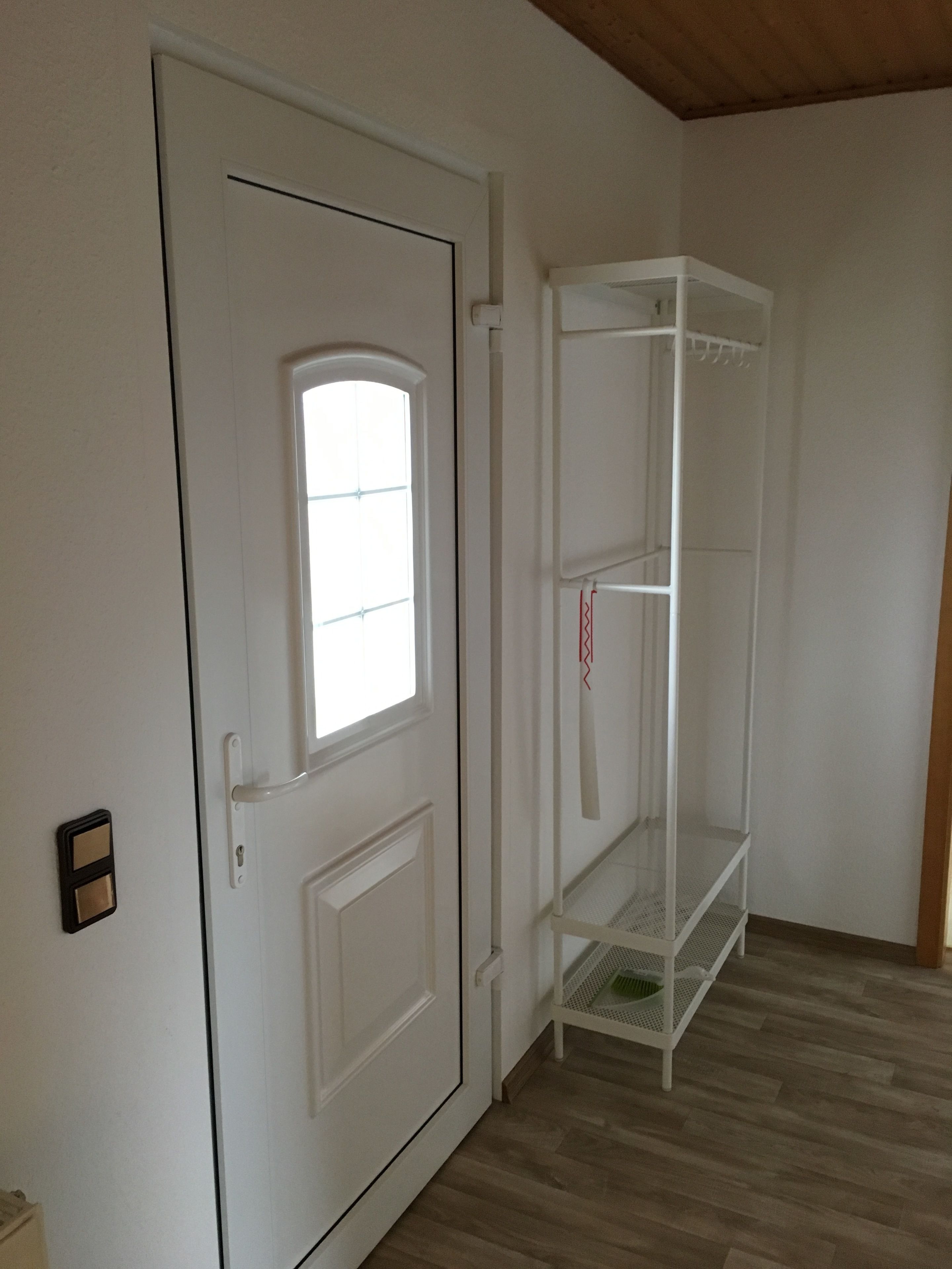 A white door with a window, a white shelving unit, and a wooden floor.