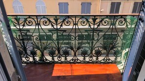 Un balcone con ringhiera in ferro battuto, pavimento in legno e vista su edifici con persiane.