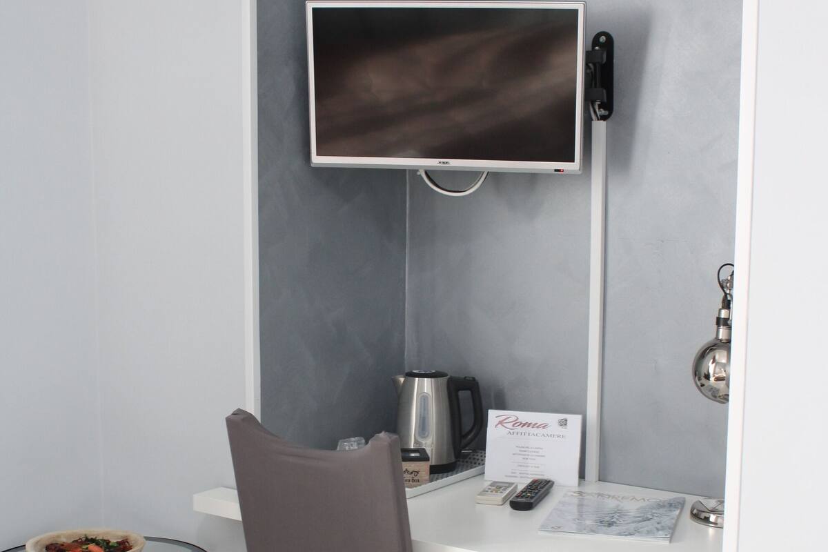 A small, modern room with a desk, chair, and a television mounted on the wall.