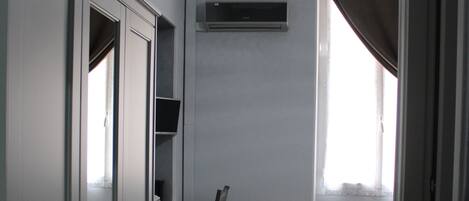 A compact room with a bed, a desk with a chair, a television, and a hanging light fixture.