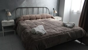 Un letto rifatto con cura, un copriletto marrone, due lampade sui comodini e una finestra con tende.