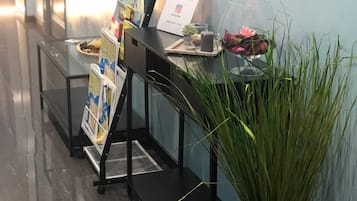 Een receptiegedeelte met een glazen displaycase, een tijdschriftrek en een potplant.