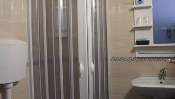 A bathroom with a shower enclosure, toilet, sink, and a mirror with shelves.