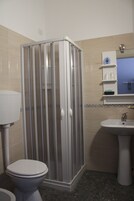 Un baño con cabina de ducha, inodoro, lavabo y un espejo con repisas.
