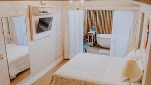 Een hotelkamer met een groot bed, een aan de muur bevestigde televisie, een badkamer achter een gordijn en een kleine tafel met een stoel.