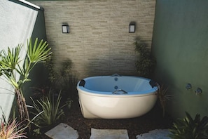 A spa area with a hot tub, surrounded by plants and a stone wall.