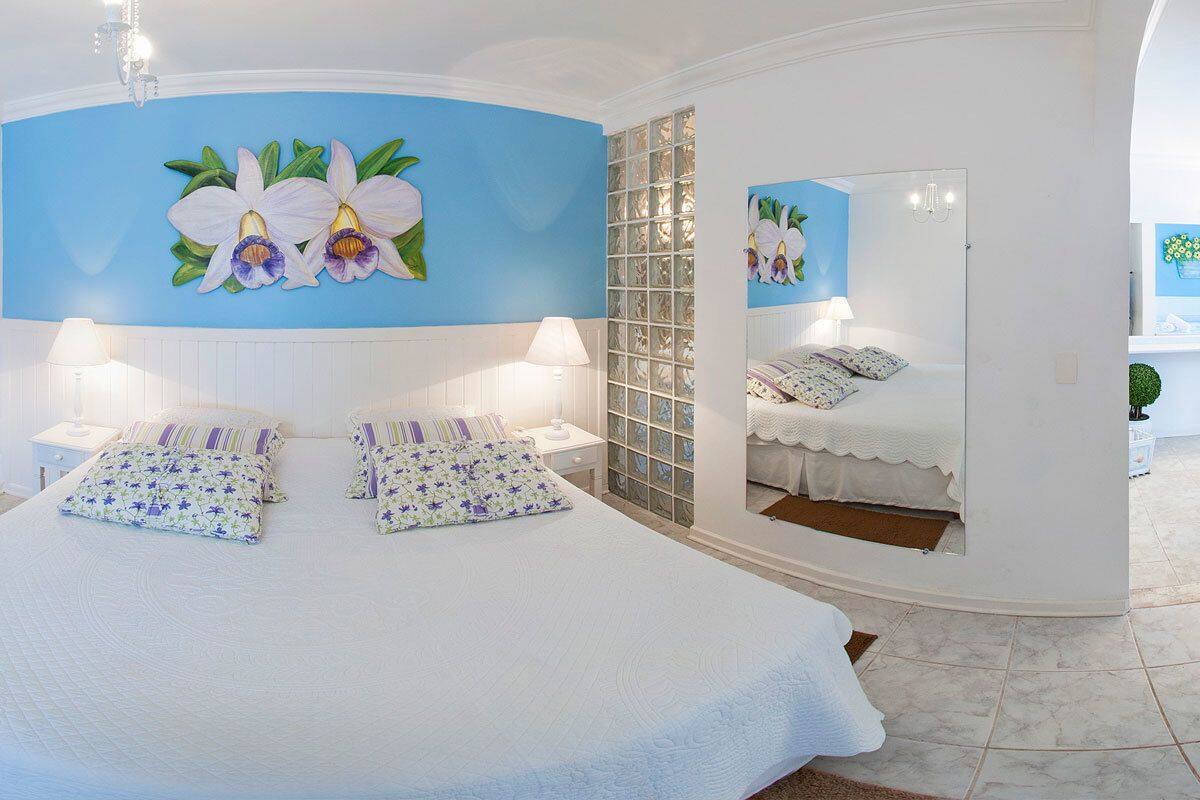 A bedroom with a large bed, two nightstands, a mirror, and orchid wall art.