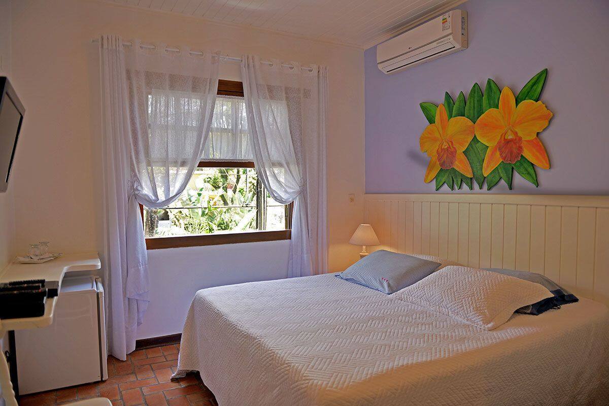 A bedroom with a bed, a desk, a chair, a window with curtains, and a wall-mounted air conditioner.