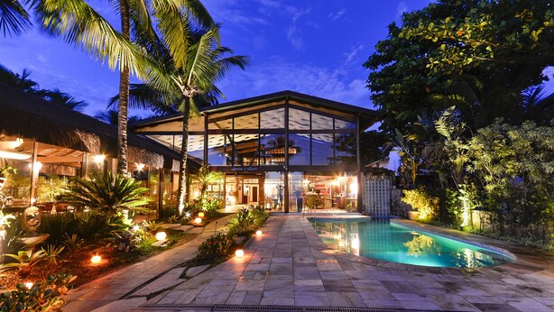 Une maison moderne dotée d’une façade en verre, d’une piscine et d’espaces extérieurs bien éclairés.