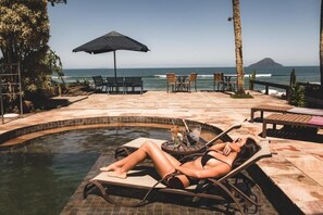 A poolside area with lounge chairs, a table with drinks, and a view of the ocean.