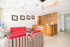 A hotel reception area with a red sofa, striped armchairs, a reception desk with a RedDoorz sign, and a wall with clocks and a framed picture. - Reddoorz Home Hotel Truong Cong Giai (Hanoi)
