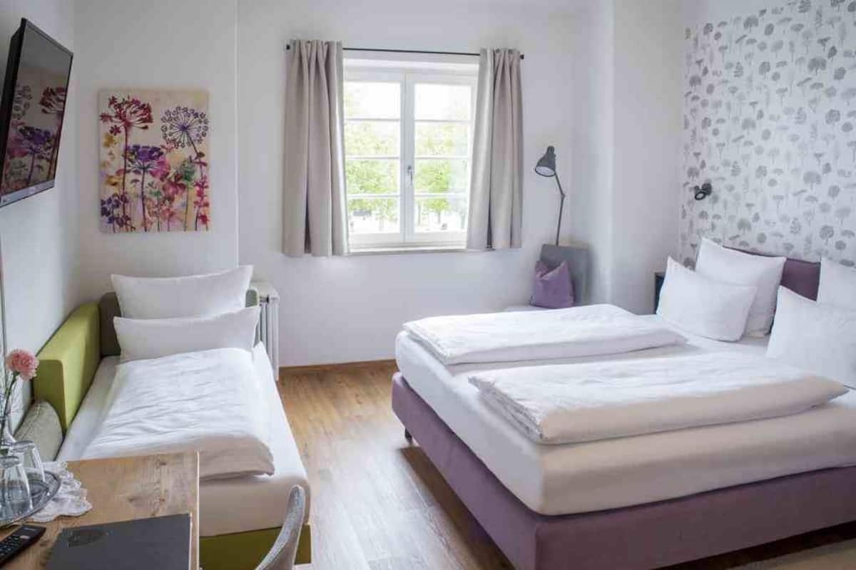 A hotel room with two beds, a desk with a computer, a lamp, and a window with curtains.