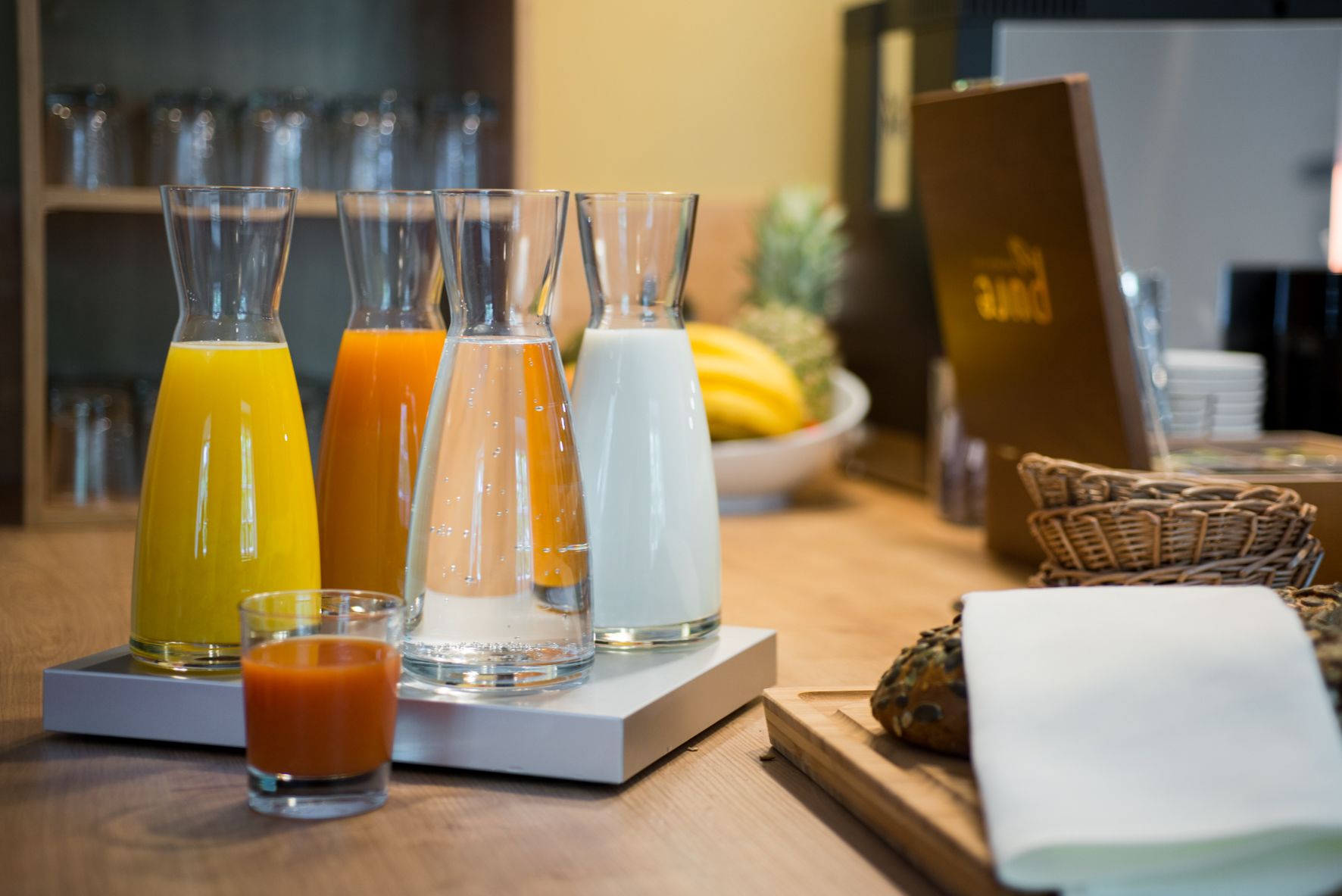 A breakfast bar with various beverages, including orange juice, milk, and a small glass of a red drink.