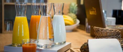A breakfast bar with various beverages, including orange juice, milk, and a small glass of a red drink.