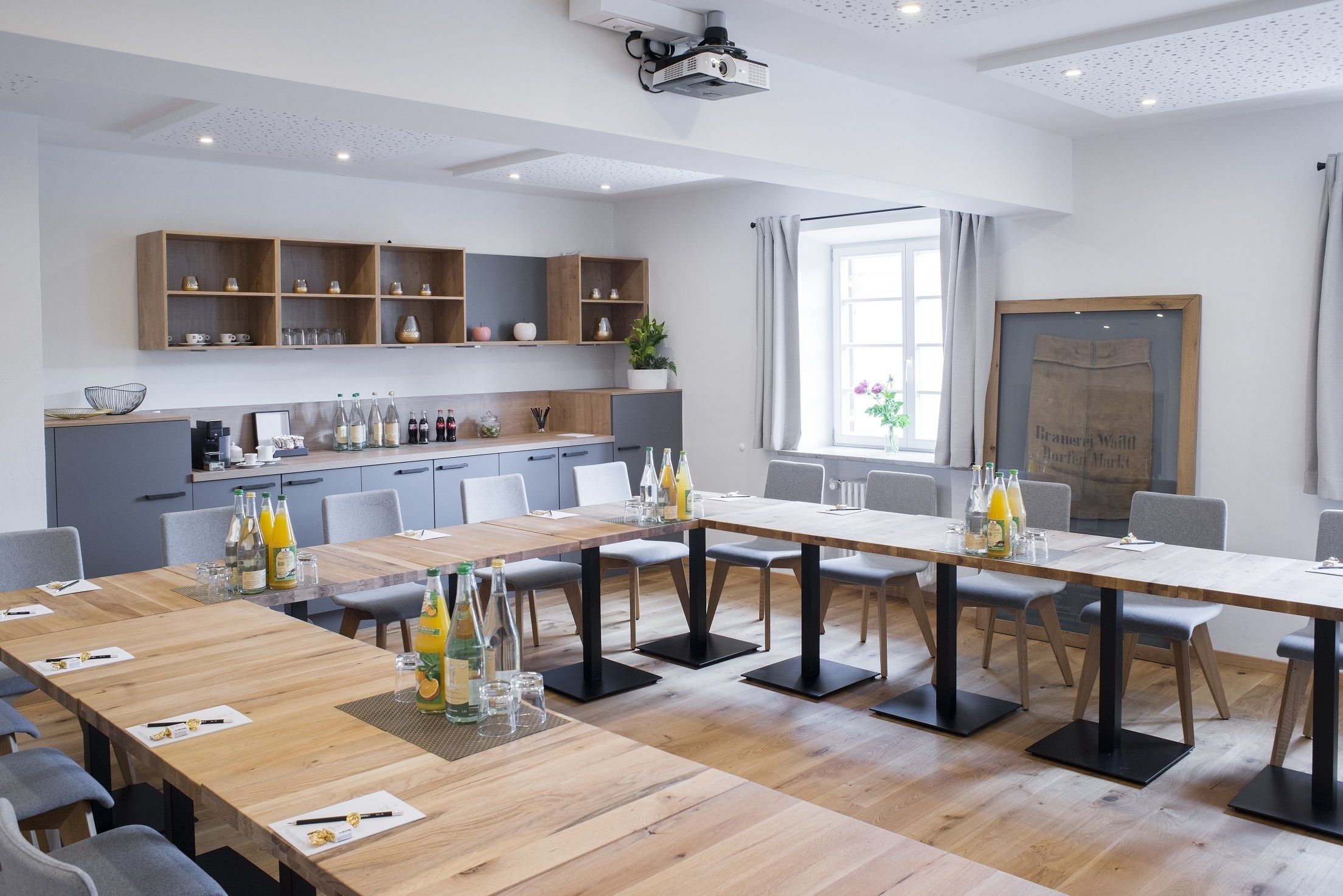 A modern kitchen with wooden shelves, a long dining table, and a projector mounted on the ceiling.