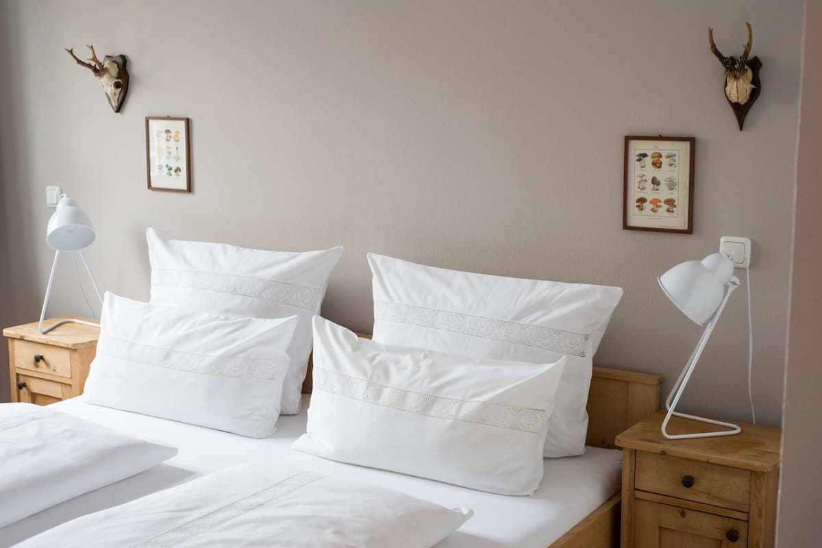 A neatly made bed with white bedding and decorative pillows, a bedside lamp, and a wooden nightstand.