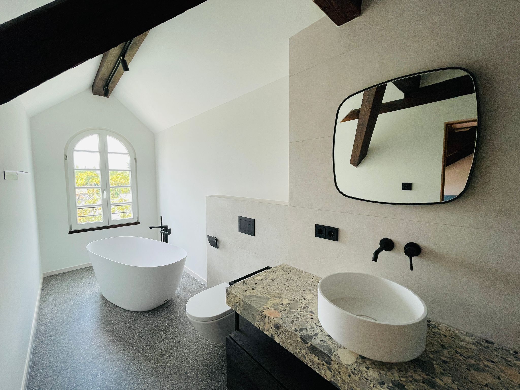 Un bagno moderno con una vasca da bagno freestanding, un water, un lavabo con piano in granito e uno specchio grande.