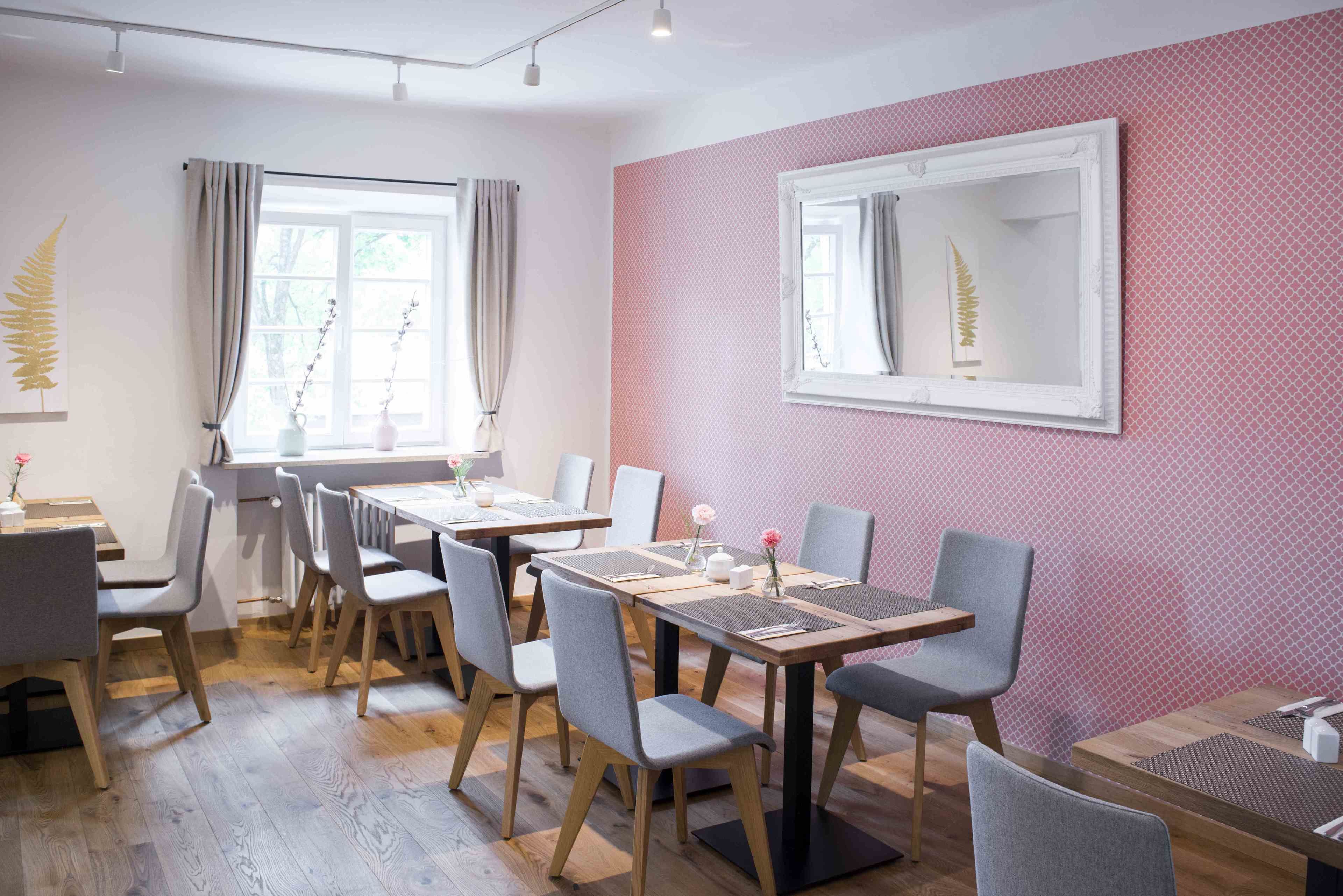 A modern dining area with wooden tables and grey chairs, a large mirror on the wall, and a pink textured wall.