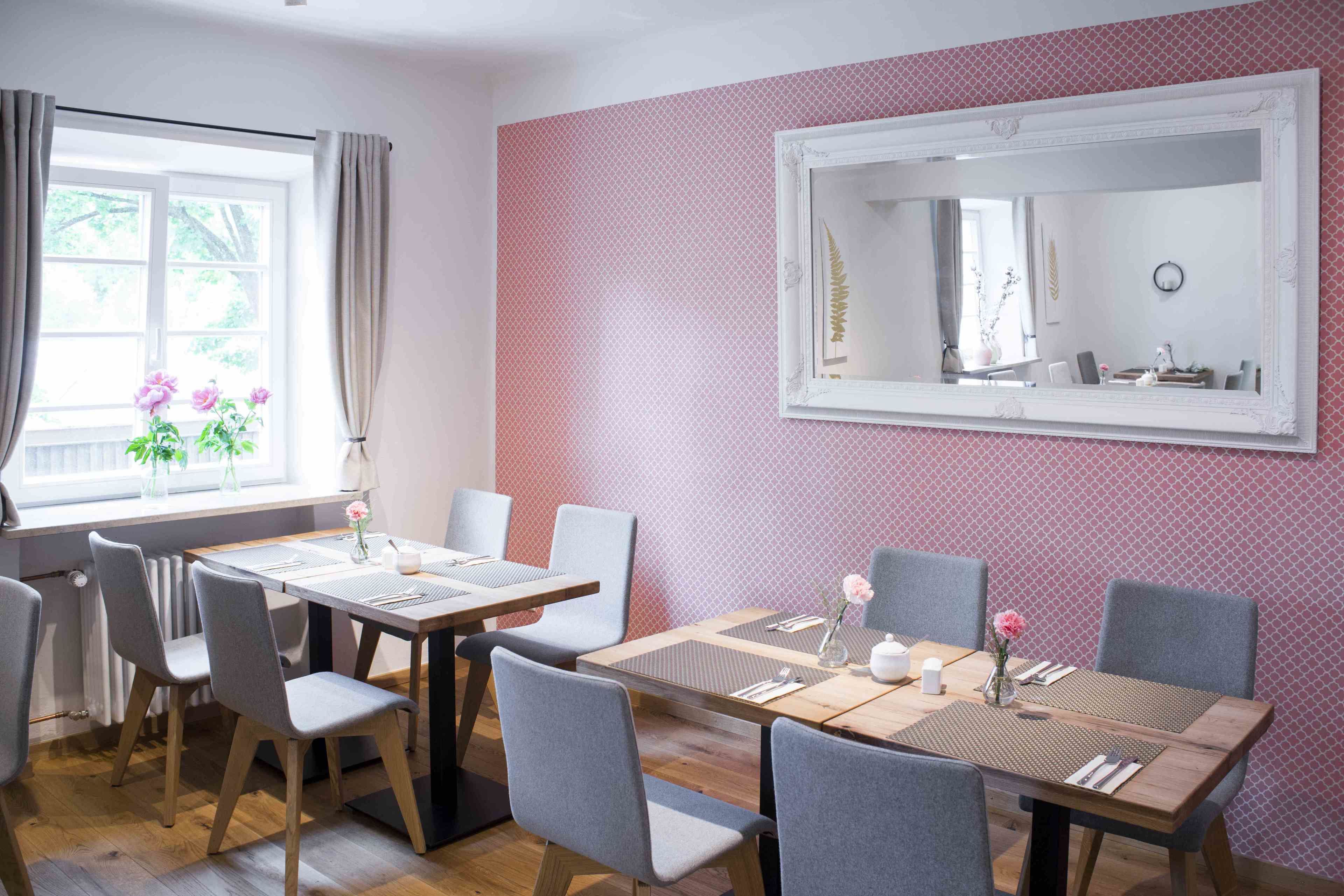Een eetruimte met een tafel voor vier personen, omringd door stoelen, een grote spiegel aan de muur en een raam met gordijnen.