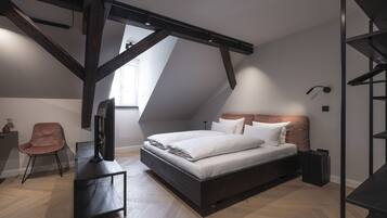 Een moderne slaapkamer met schuine plafonds, een bed met witte lakens, een bureau met een computer en een stoel.