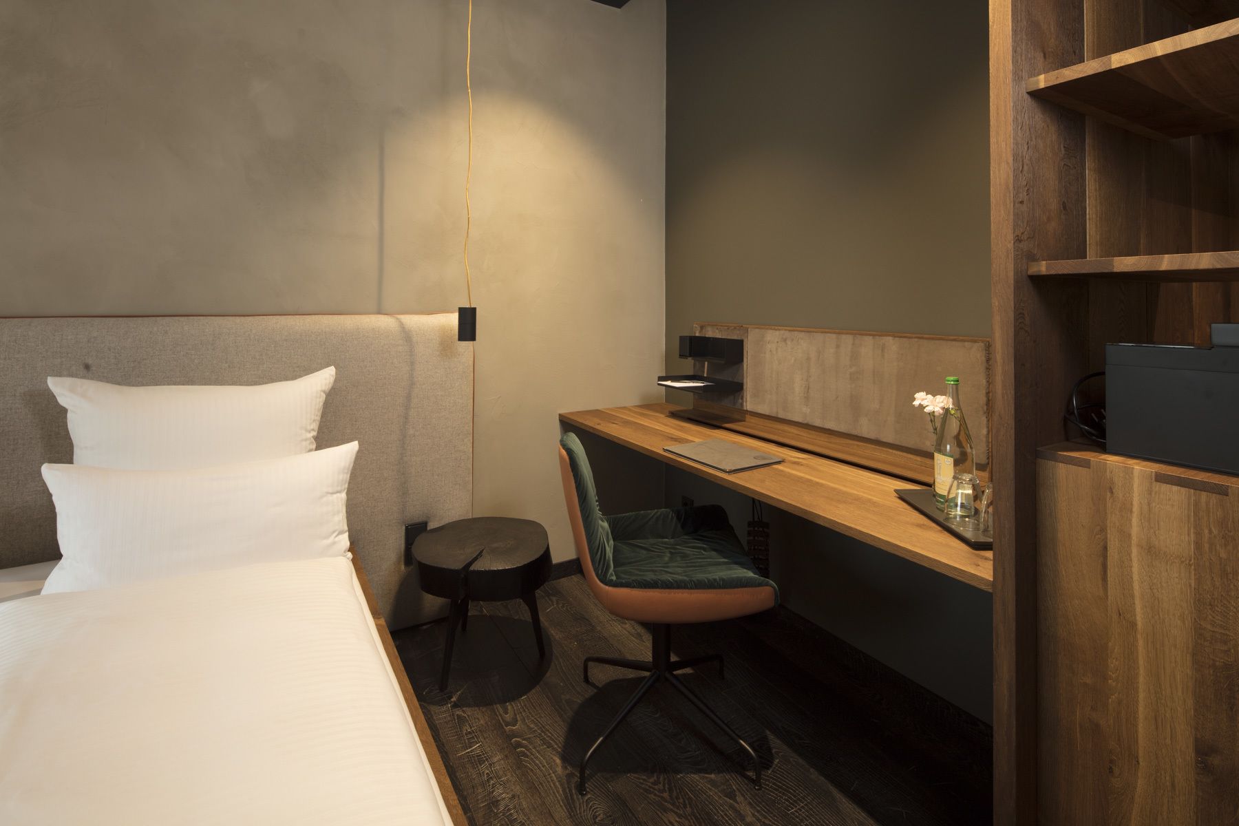 A hotel room with a bed, a desk, a chair, and a small table with a bottle and glasses.