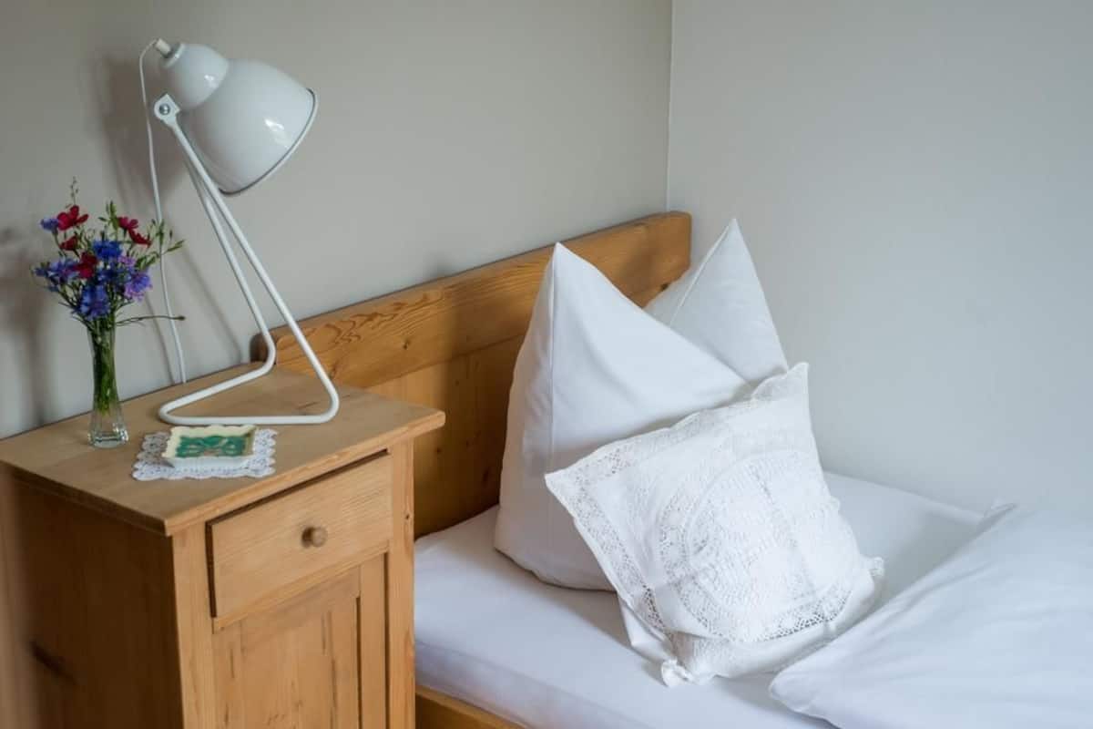 A neatly made bed with white linens, a wooden nightstand with a white lamp, and a vase with flowers.