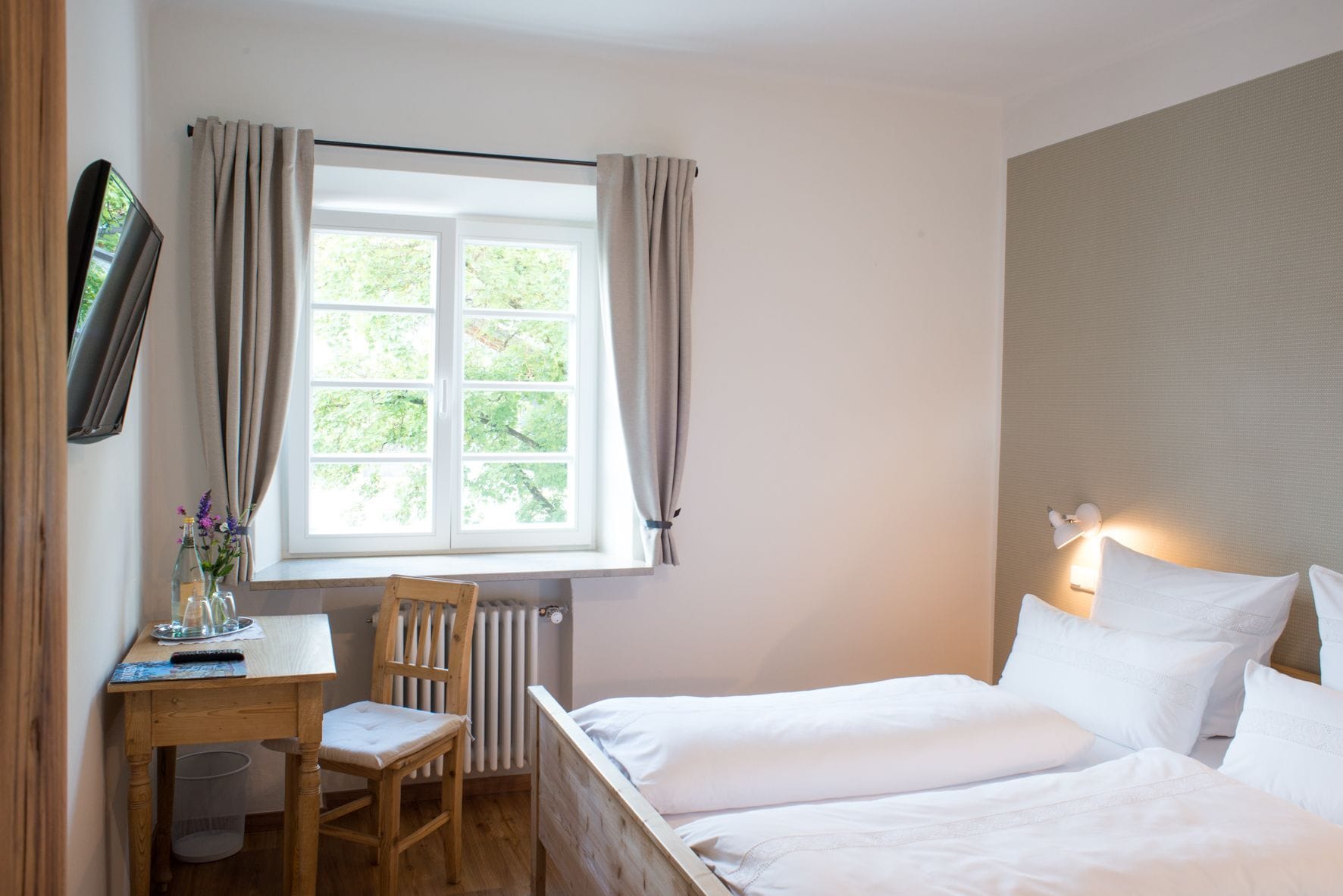 A bedroom with a bed, a desk, a chair, a radiator, and a window with curtains.