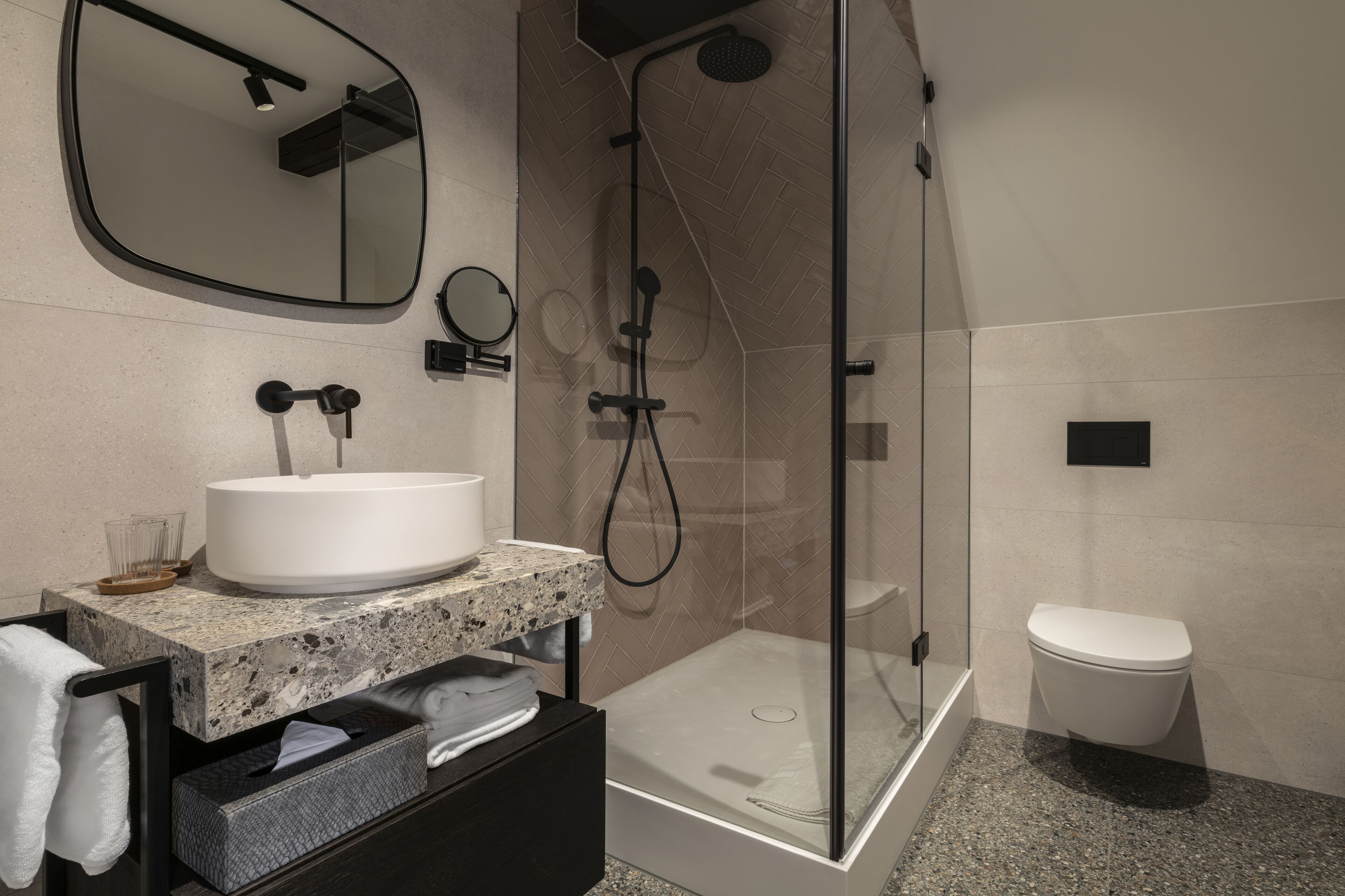 Un baño moderno con lavamanos de granito, ducha con cerramiento de vidrio y inodoro blanco.