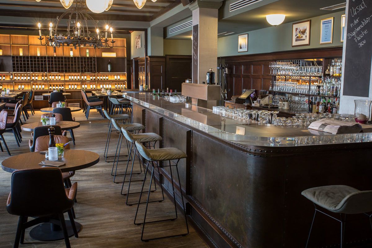 A bar area with a long counter, stools, and a variety of bottles and glasses.