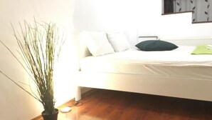 Une chambre avec un lit blanc, un oreiller vert et une plante en pot.