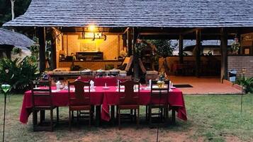 An outdoor dining area with tables set for a meal, a covered seating area, and a brick building in the background.