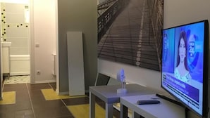 A modern living room with a large painting of a bridge, a flat-screen TV, and a white bench. - New Central Roof Top (Bucharest)
