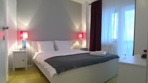 A neatly arranged hotel room with a bed, bedside lamps, a nightstand, a window with curtains, and a small table with a lamp. - New Central Roof Top (Bucharest)