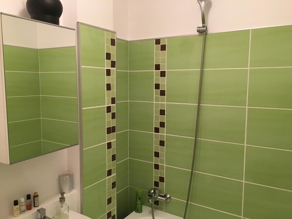 A bathroom with green tiles, a shower, a sink, and a mirror.