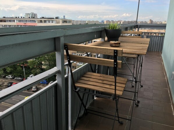 A balcony with a wooden table and chairs, a potted plant, and a view of the cityscape. - New Central Roof Top (Bucharest)