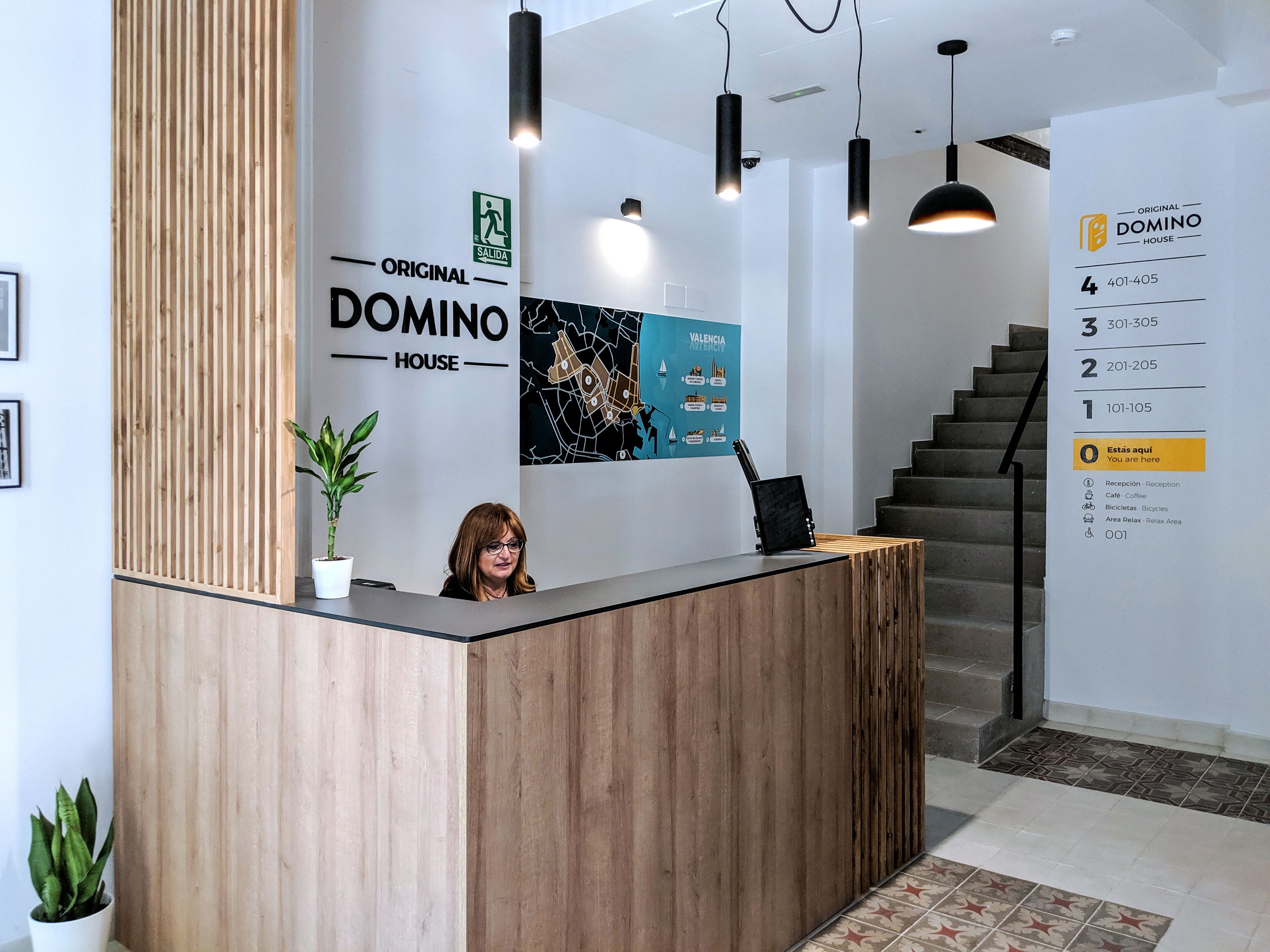 Un mostrador de recepción con detalles de madera, una planta en maceta y un cartel que indica la ubicación de Original Domino House.