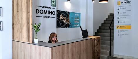 Un mostrador de recepción con detalles de madera, una planta en maceta y un cartel que indica la ubicación de Original Domino House.