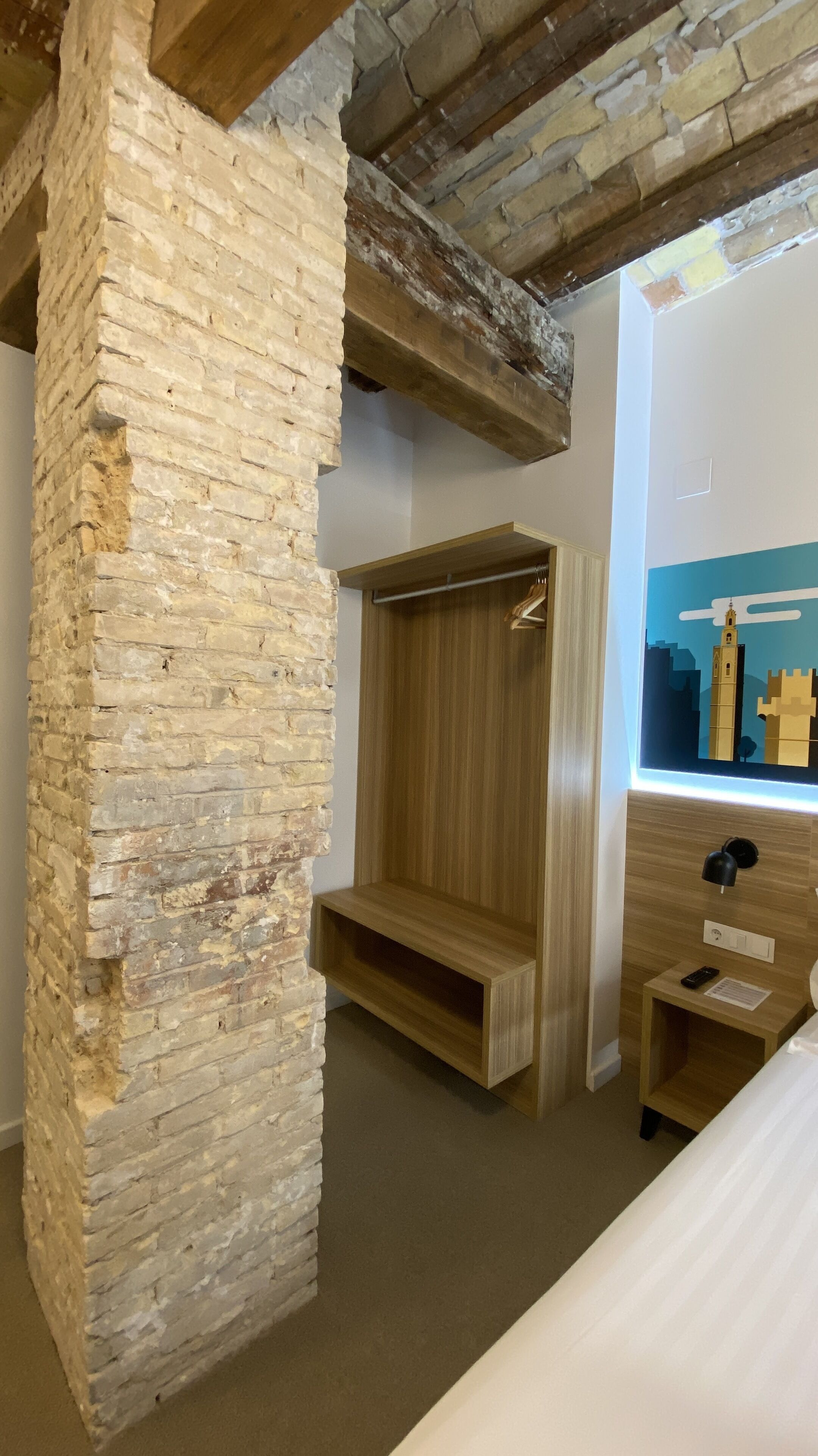 Ein Zimmer mit freiliegenden Backsteinwänden, einem Holzschrank und einem Bett mit Kopfteil.