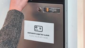 Una mano presionando un botón en un lector de tarjetas, con la leyenda 'PLACE YOUR KEY HERE' y un plano que muestra rutas de evacuación e instrucciones de emergencia.