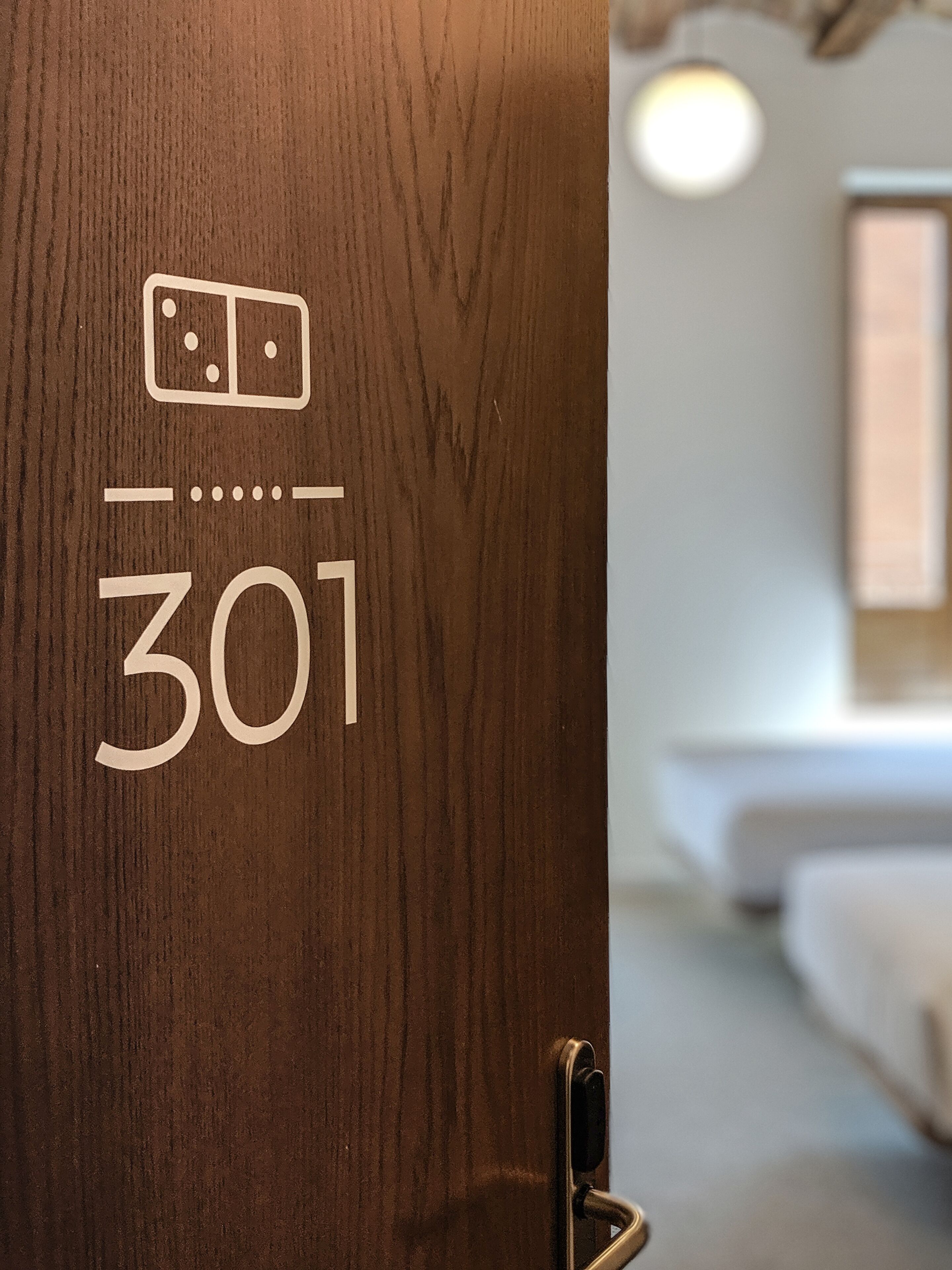 A wooden door with a room number 301 and a bed in the background.