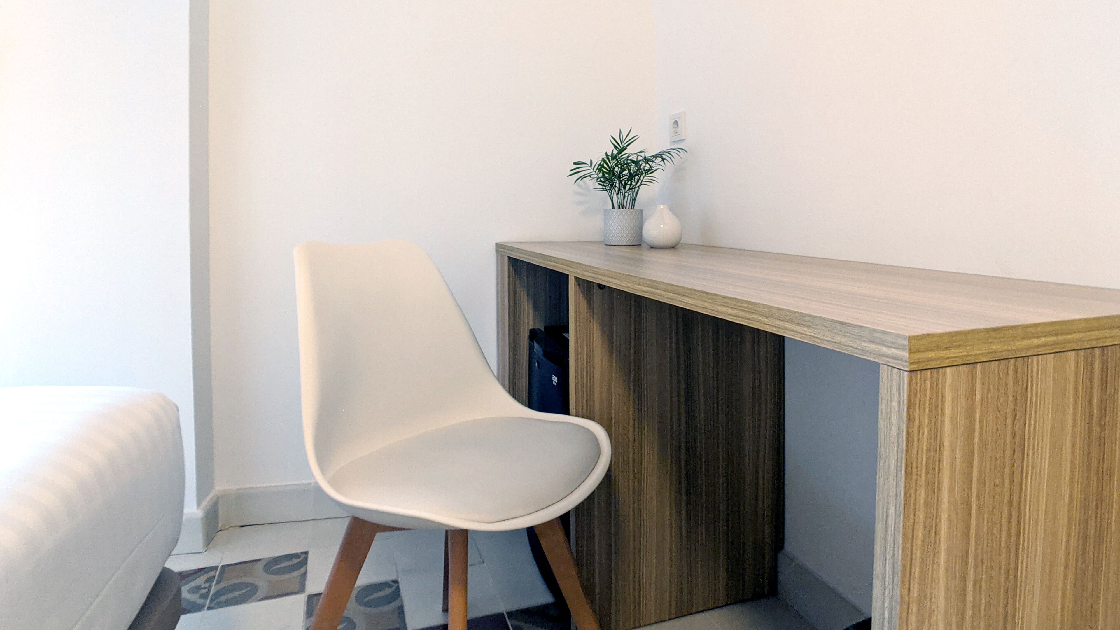 A modern room with a white chair, a wooden desk, and a small plant on the desk.