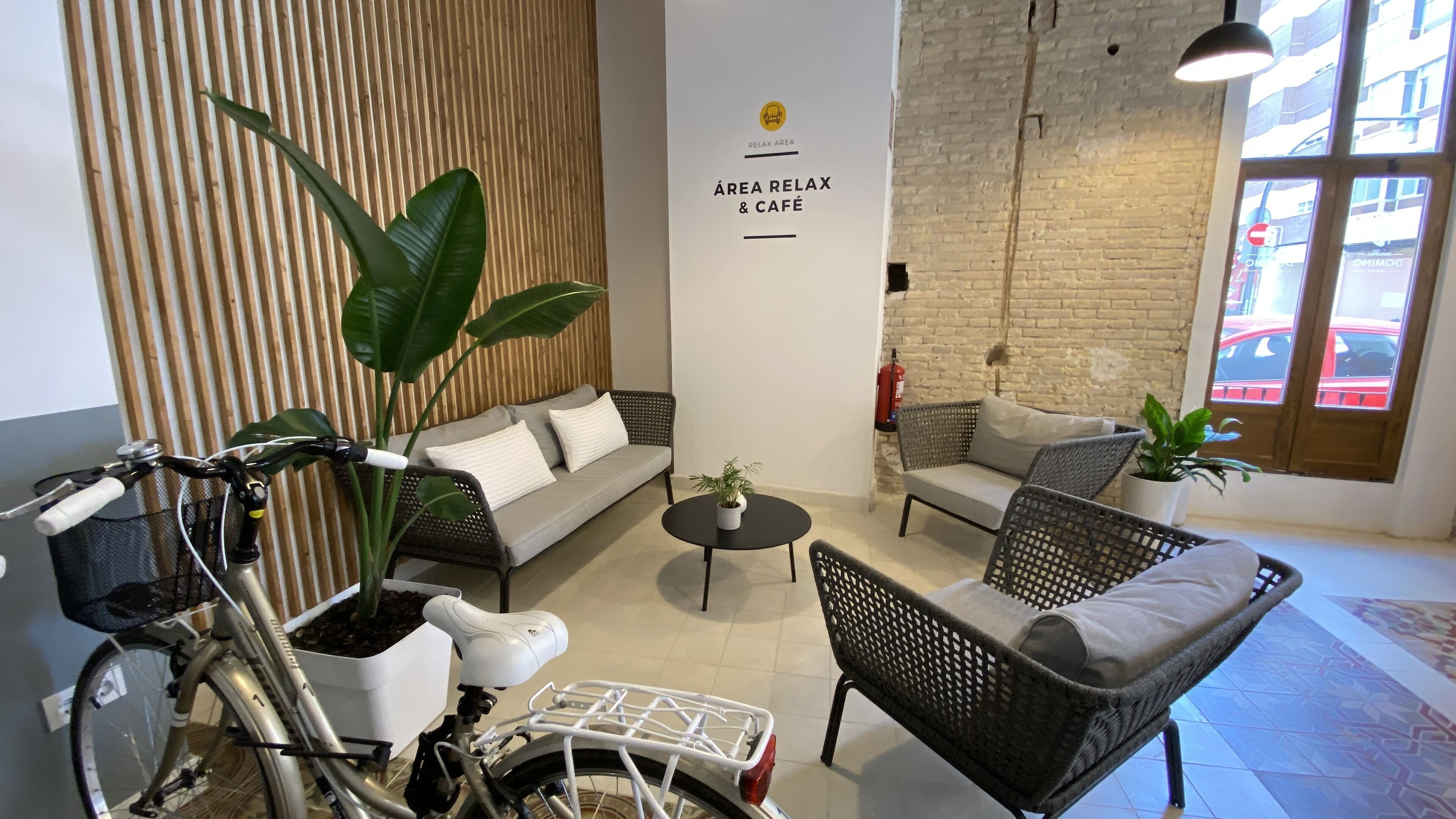 A cozy seating area with a sofa, chairs, and a bicycle. A sign reads "AREA RELAX & CAFÉ".