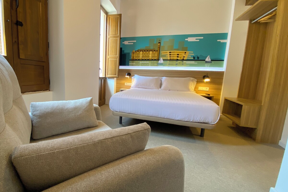 A bedroom with a bed, a sofa, and a painting of a cityscape.